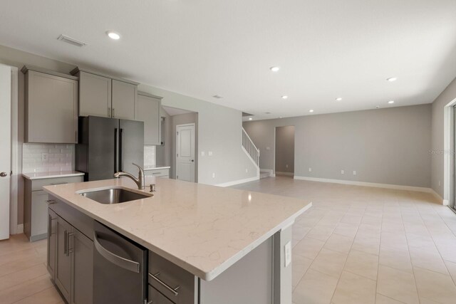 kitchen with light stone counters, sink, a center island with sink, gray cabinets, and appliances with stainless steel finishes