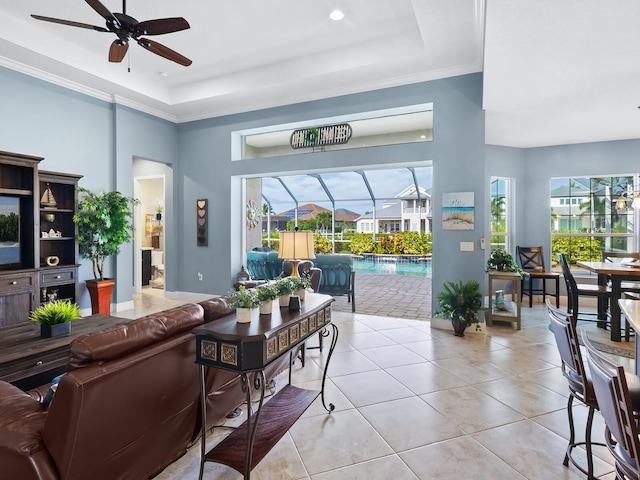 living room featuring light tile patterned flooring, crown molding, ceiling fan, a tray ceiling, and a high ceiling