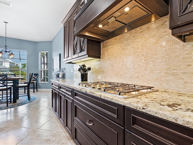 kitchen featuring stainless steel gas stovetop, tasteful backsplash, custom exhaust hood, dark brown cabinets, and decorative light fixtures