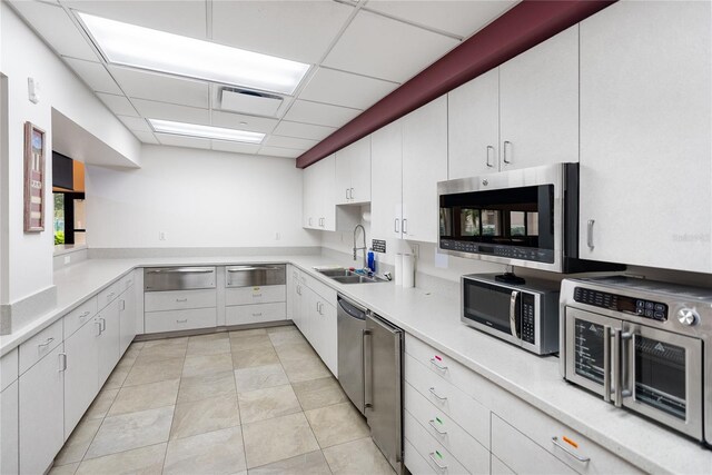 kitchen with white cabinetry, sink, stainless steel appliances, a paneled ceiling, and light tile patterned flooring