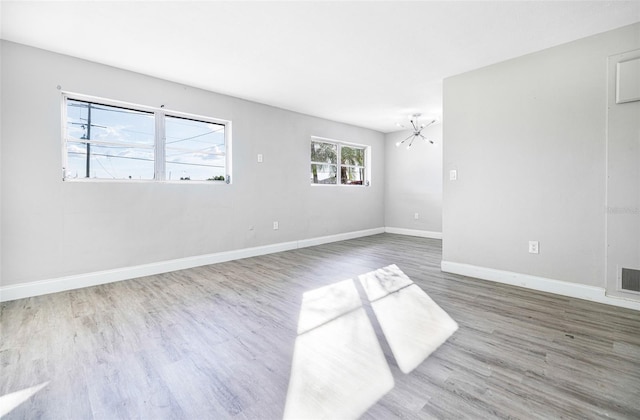 empty room with hardwood / wood-style flooring, a notable chandelier, and a healthy amount of sunlight