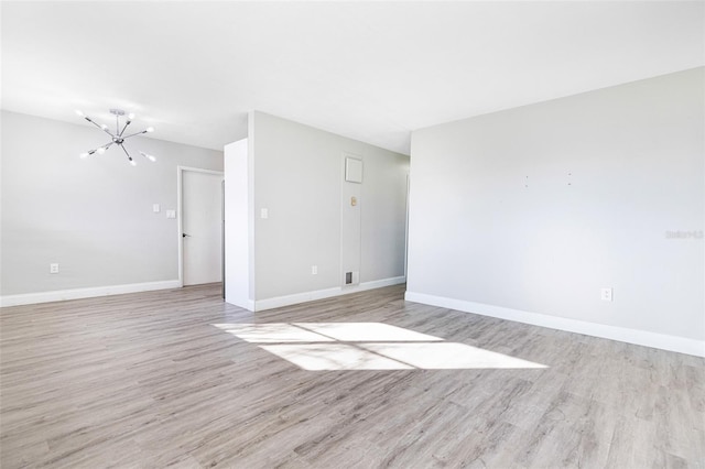 empty room with light hardwood / wood-style flooring and a chandelier