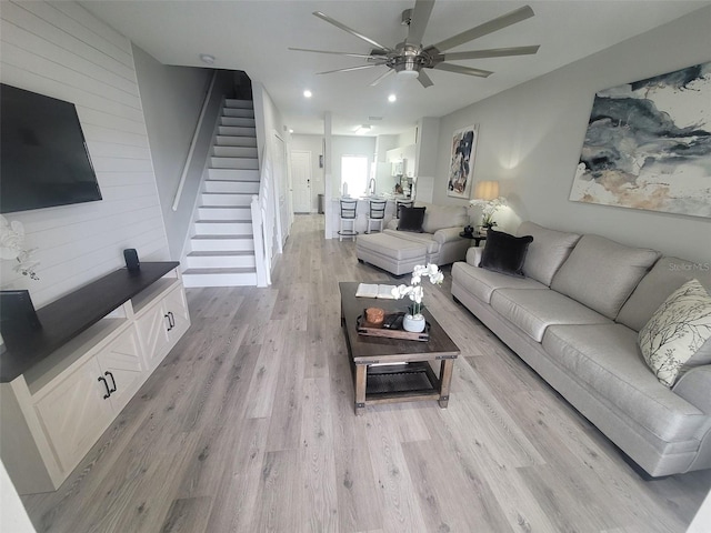 living room with light wood-type flooring, wood walls, and ceiling fan