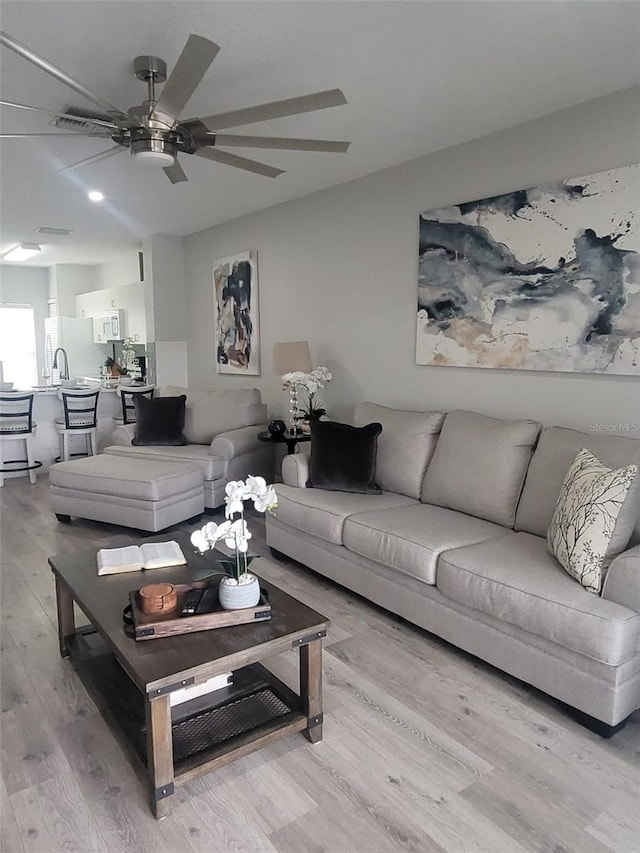 living room with ceiling fan, light hardwood / wood-style flooring, and sink