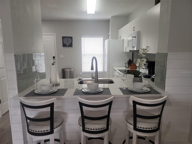 kitchen with a breakfast bar, a textured ceiling, sink, white cabinets, and white appliances