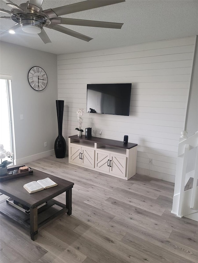 living room featuring ceiling fan, a textured ceiling, and light hardwood / wood-style flooring