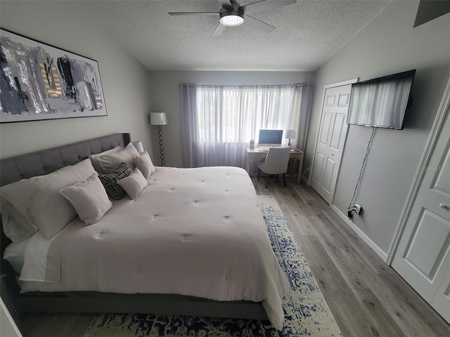 bedroom with light hardwood / wood-style floors, vaulted ceiling, a closet, a textured ceiling, and ceiling fan