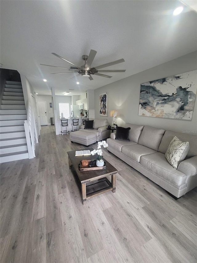 living area with stairs, wood finished floors, and a ceiling fan