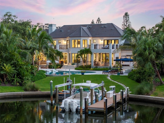 back house at dusk featuring a balcony, a patio, a yard, and a water view