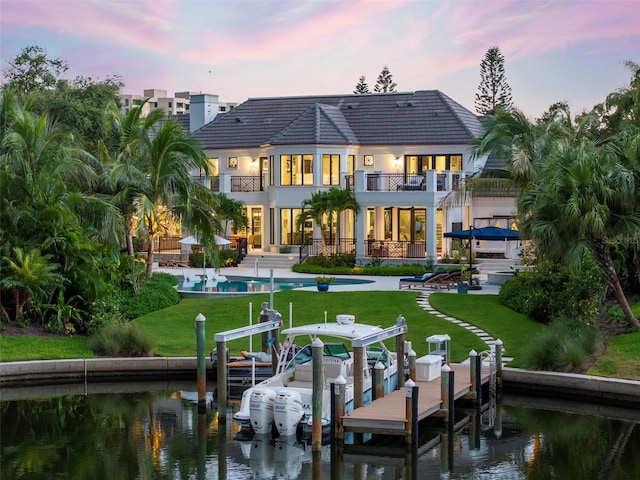 501 Harbor Point Rd, Longboat Key, FL 34228 - back of property at dusk featuring a balcony, a water view, a patio, and a lawn