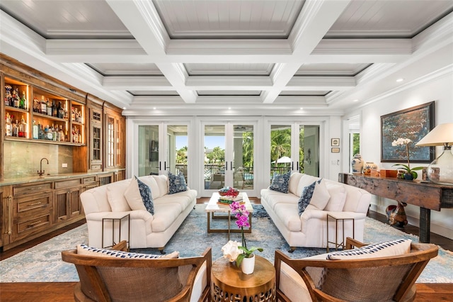 living room with beamed ceiling, dark wood-type flooring, coffered ceiling, ornamental molding, and wet bar