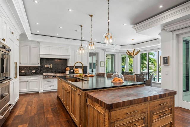 kitchen featuring a large island with sink, dark wood-type flooring, white cabinets, crown molding, and sink