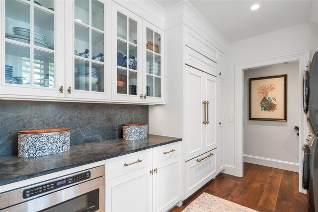 501 Harbor Point Rd, Longboat Key, FL 34228 - bar featuring stacked washing machine and dryer, dark wood-type flooring, wall oven, tasteful backsplash, and baseboards