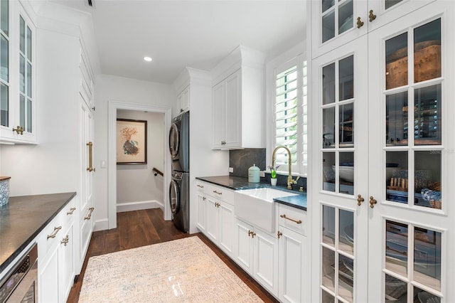 kitchen featuring decorative backsplash, stacked washing maching and dryer, white cabinetry, dark hardwood / wood-style floors, and sink