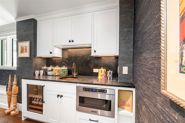 kitchen with sink, white cabinets, beverage cooler, crown molding, and stainless steel oven