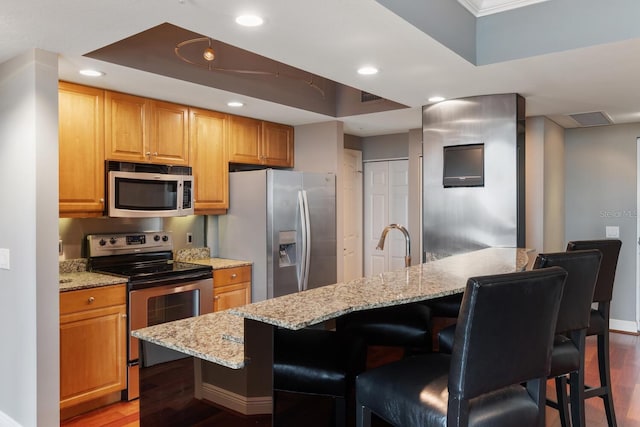 kitchen featuring a kitchen island with sink, a breakfast bar area, appliances with stainless steel finishes, hardwood / wood-style floors, and light stone countertops