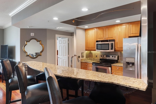 kitchen with light stone counters, a kitchen bar, stainless steel appliances, and hardwood / wood-style flooring