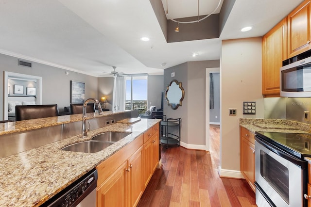 kitchen with light stone counters, ornamental molding, sink, hardwood / wood-style flooring, and appliances with stainless steel finishes