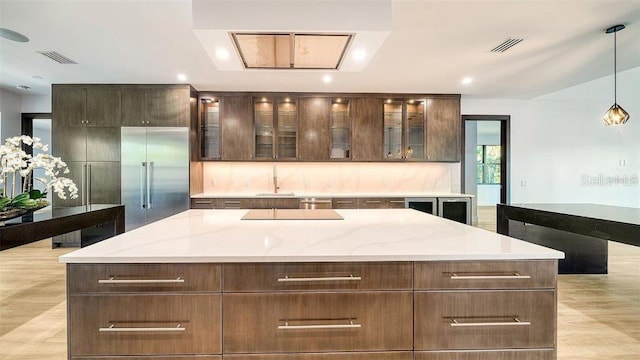 kitchen with built in fridge, a kitchen island, pendant lighting, light stone countertops, and light hardwood / wood-style floors