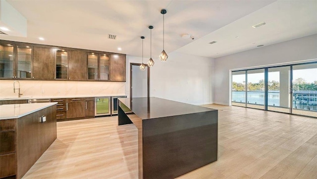 kitchen with a kitchen island, backsplash, pendant lighting, light wood-type flooring, and wine cooler