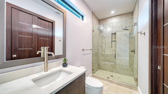 bathroom featuring toilet, vanity, tile patterned flooring, and a shower with door