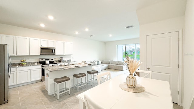 kitchen with white cabinets, a kitchen island with sink, stainless steel appliances, and a kitchen bar