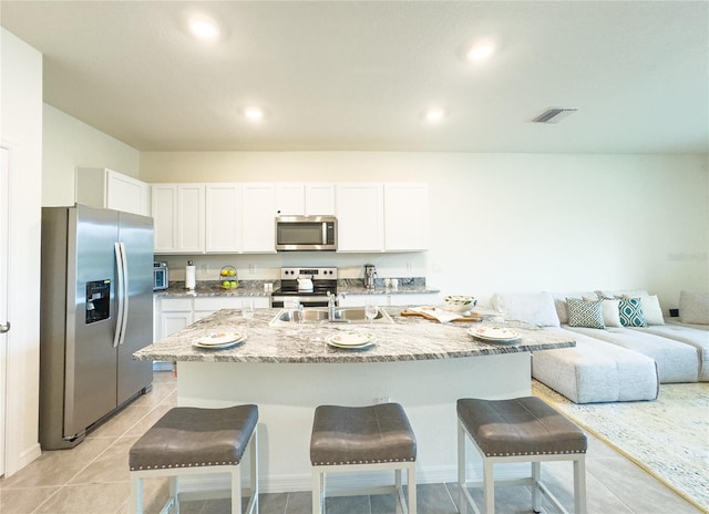 kitchen featuring light tile patterned floors, appliances with stainless steel finishes, white cabinetry, a kitchen island with sink, and a kitchen bar