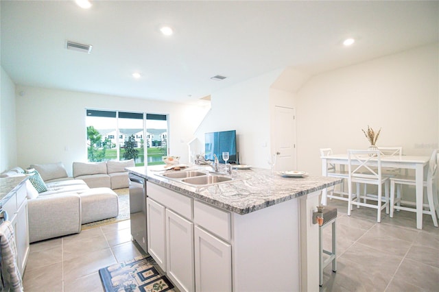 kitchen featuring sink, dishwasher, white cabinets, light tile patterned floors, and a center island with sink