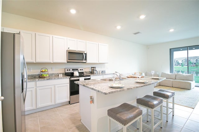 kitchen with a center island with sink, appliances with stainless steel finishes, light stone counters, and white cabinetry