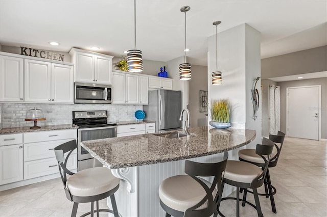 kitchen featuring white cabinets, appliances with stainless steel finishes, dark stone countertops, sink, and decorative light fixtures