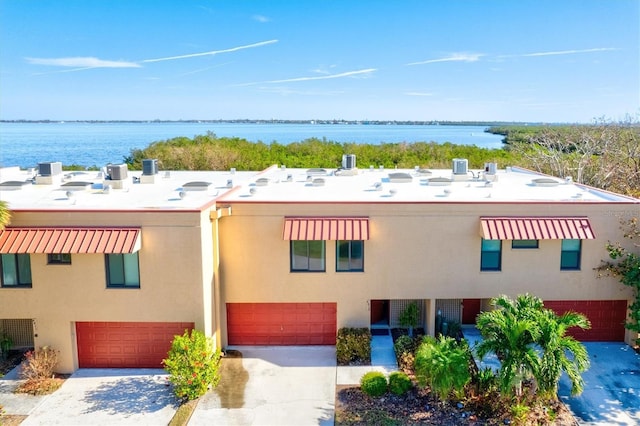 exterior space featuring stucco siding, a water view, concrete driveway, and a garage