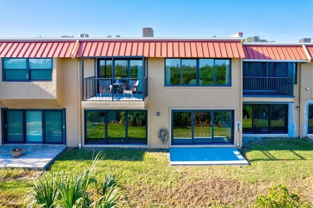 back of property featuring a lawn, metal roof, a balcony, and stucco siding