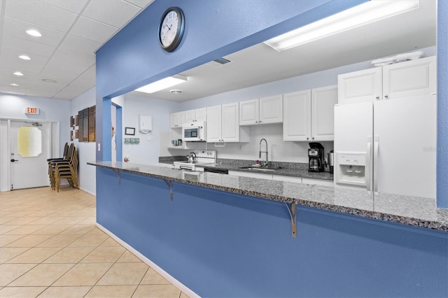 kitchen with kitchen peninsula, sink, a kitchen bar, white cabinetry, and white appliances