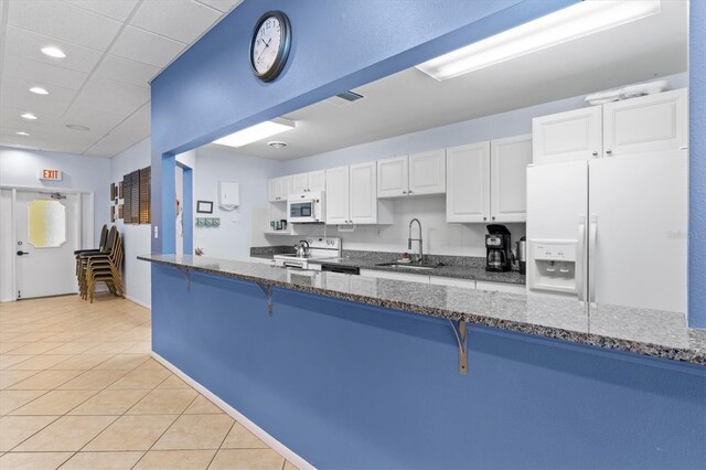 kitchen featuring a breakfast bar area, a sink, light tile patterned floors, white cabinets, and white appliances