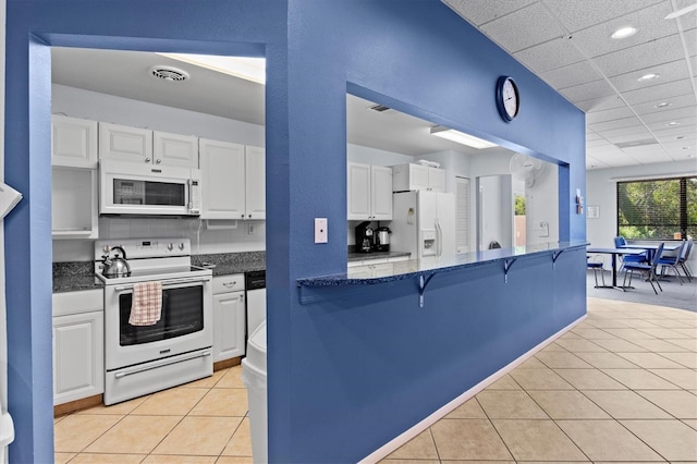 kitchen with a breakfast bar, white appliances, white cabinetry, light tile patterned floors, and visible vents