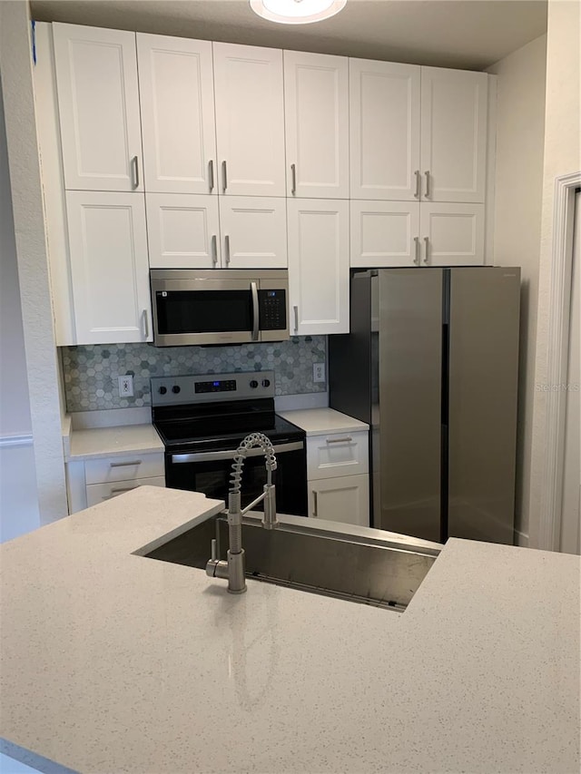 kitchen featuring appliances with stainless steel finishes, white cabinetry, light stone counters, and tasteful backsplash