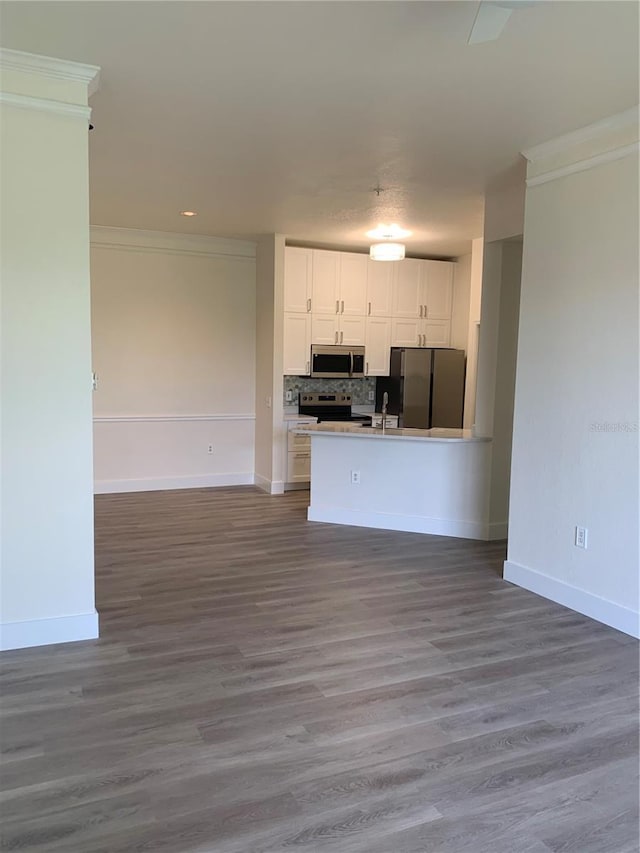 kitchen featuring white cabinetry, open floor plan, appliances with stainless steel finishes, backsplash, and crown molding