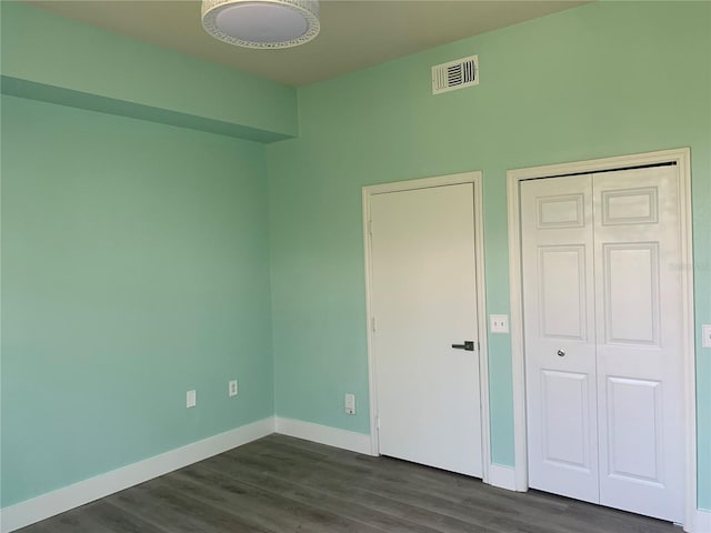 unfurnished bedroom with baseboards, visible vents, dark wood finished floors, and a closet