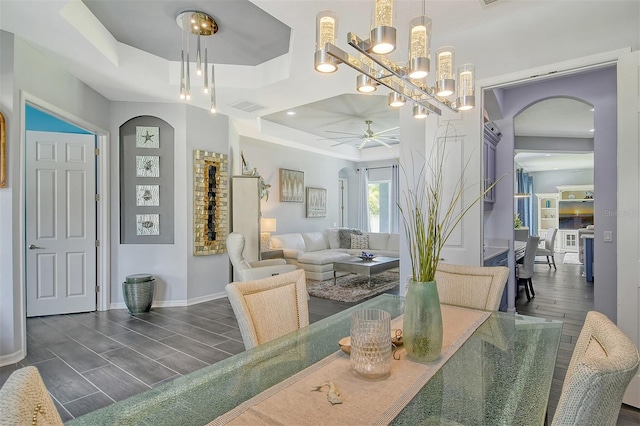 dining space with ceiling fan with notable chandelier, dark hardwood / wood-style floors, and a raised ceiling