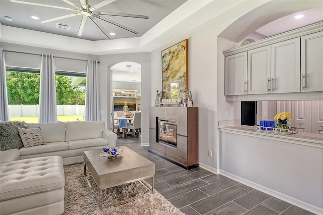 living room featuring ceiling fan, a fireplace, and dark wood-type flooring