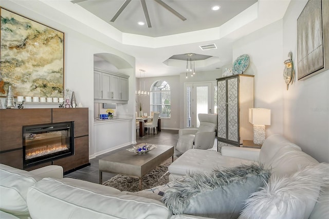 living room with a raised ceiling, ceiling fan, and dark hardwood / wood-style floors