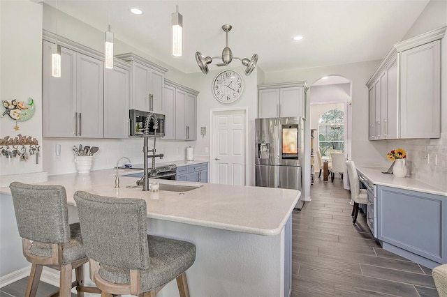 kitchen with hanging light fixtures, dark hardwood / wood-style floors, a kitchen bar, kitchen peninsula, and stainless steel appliances