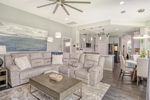 living room with ceiling fan with notable chandelier and dark hardwood / wood-style floors