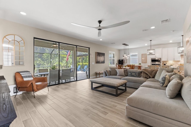 living room with ceiling fan with notable chandelier and light wood-type flooring