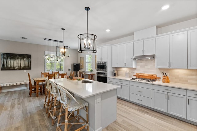 kitchen with hanging light fixtures, a center island with sink, a kitchen bar, light hardwood / wood-style flooring, and stainless steel appliances