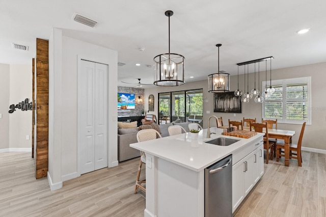 kitchen with a kitchen island with sink, sink, pendant lighting, white cabinets, and light hardwood / wood-style floors