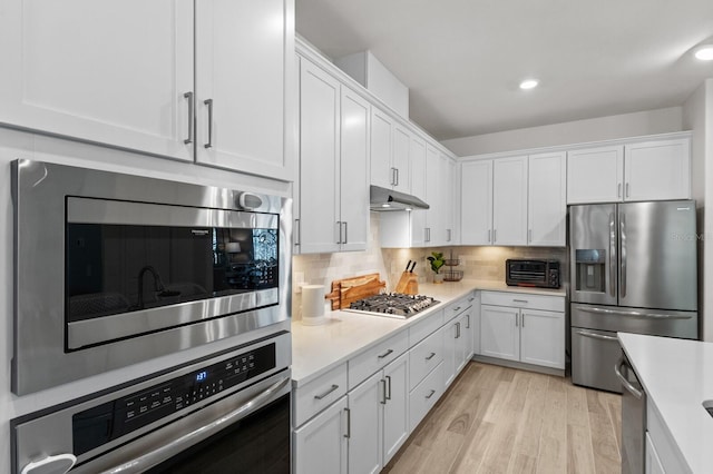 kitchen with light hardwood / wood-style floors, appliances with stainless steel finishes, decorative backsplash, and white cabinets