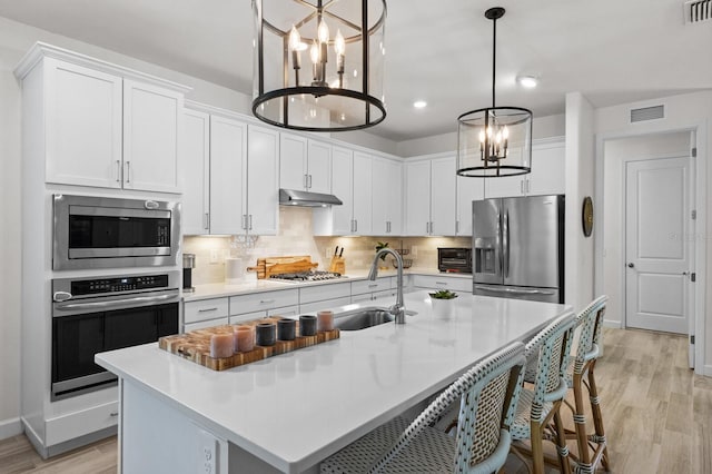 kitchen featuring appliances with stainless steel finishes, light hardwood / wood-style flooring, white cabinetry, and a center island with sink