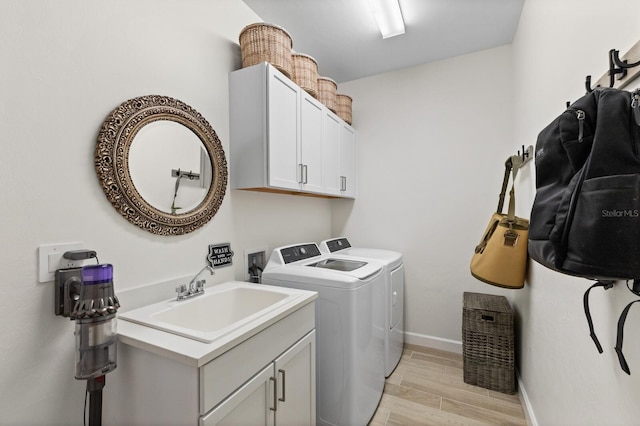 clothes washing area featuring light hardwood / wood-style floors, sink, cabinets, and washer and clothes dryer