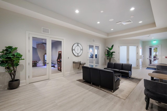 living room featuring french doors, light hardwood / wood-style flooring, and a raised ceiling